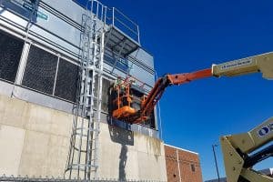 Two service technicians in a crane servicing an HVAC system on the side of a building.