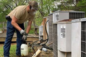 HVAC technician spraying herbicide on weeds around an HVAC system.