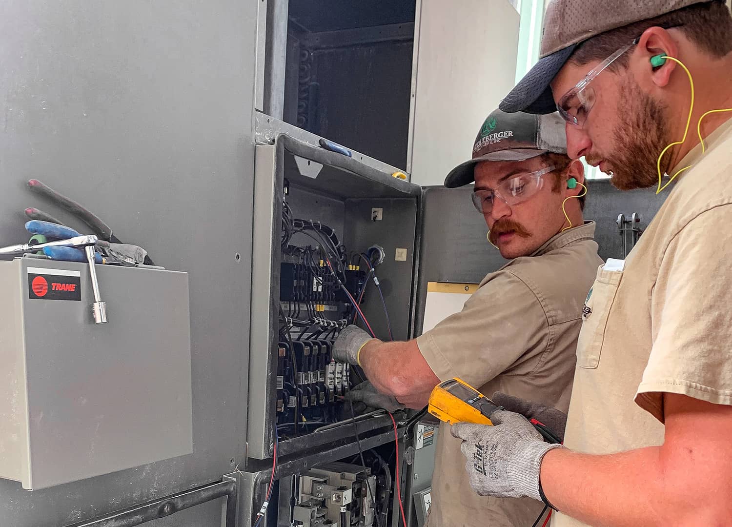 Two service technicians testing the voltage of HVAC equipment.