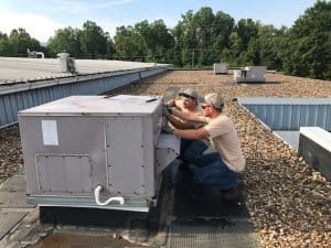 Two HVAC technicians working on a rooftop HVAC unit.