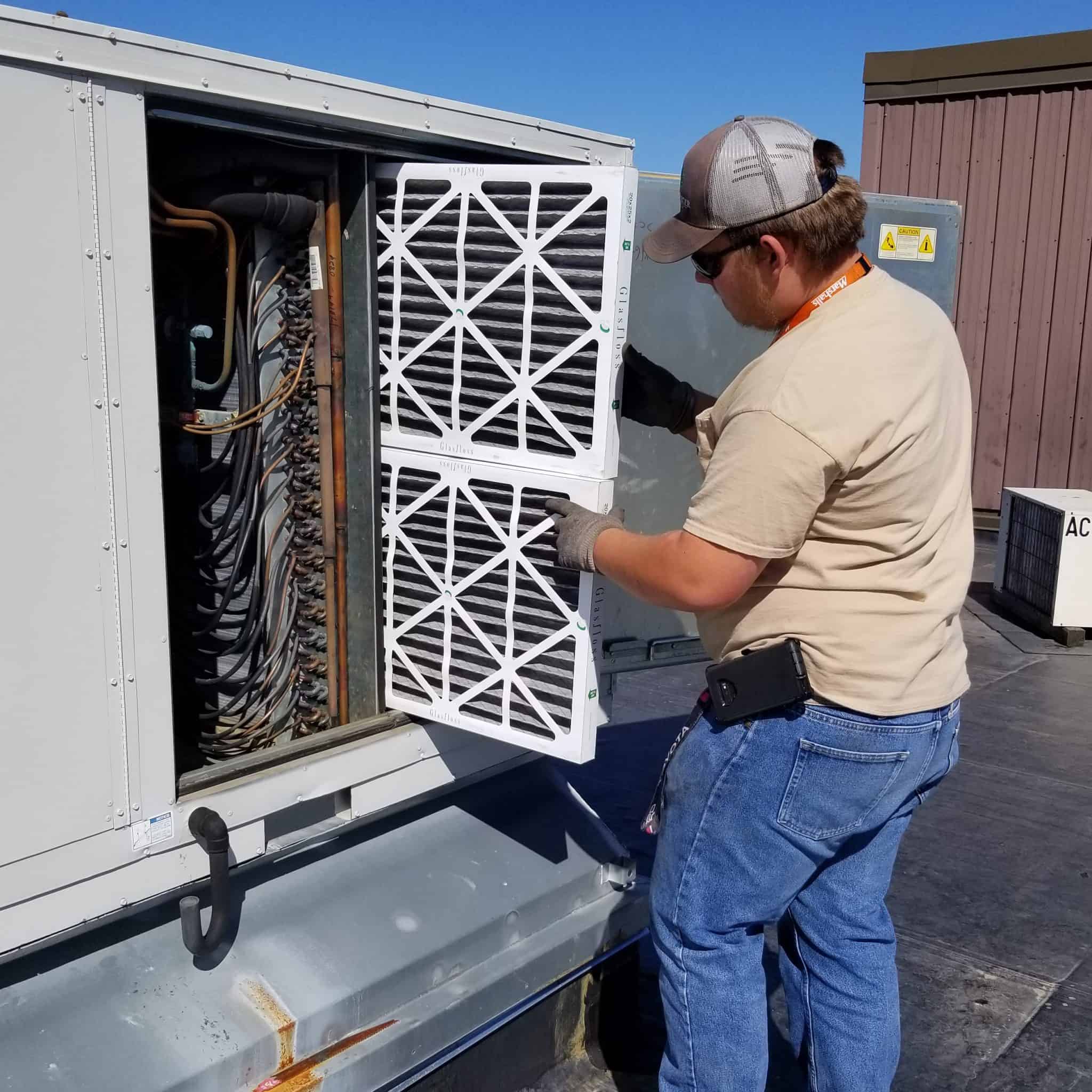 An HVAC technician replacing an air filter in an HVAC unit.
