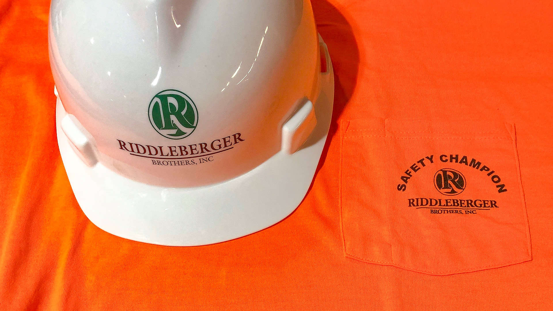 RBI hardhat on top of and RBI neon orange Safety Champion shirt