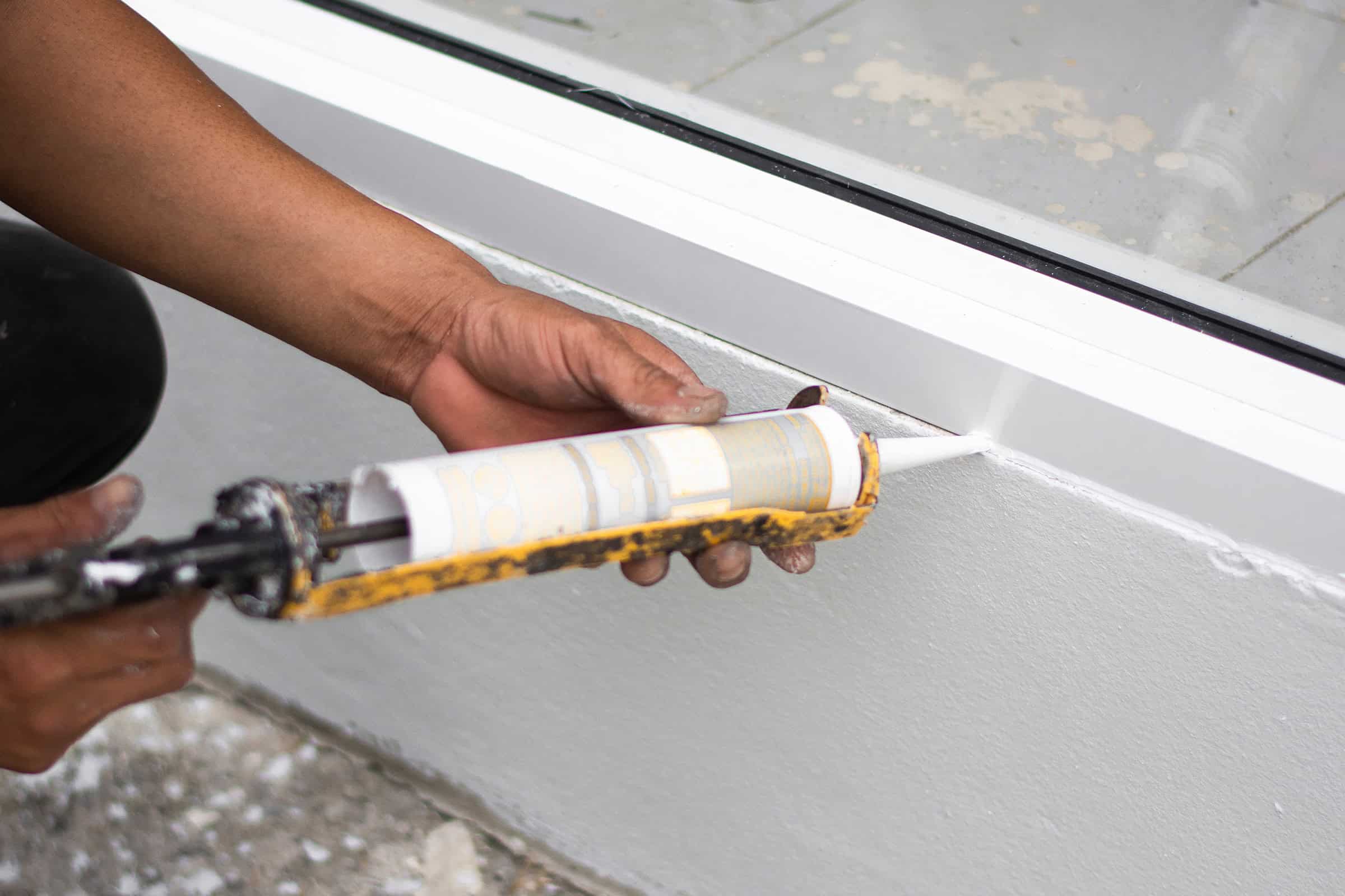 A person applying caulk in the crack around a window.