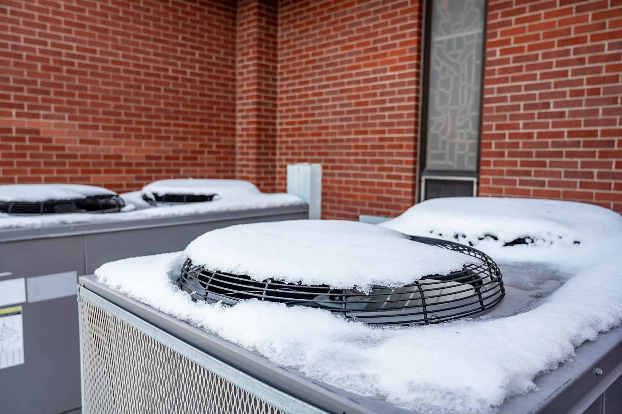 Snow on top of HVAC units outside of a brick building