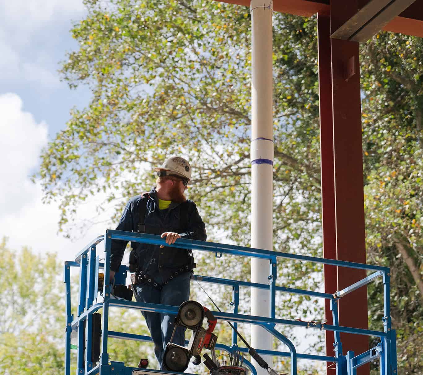 RBI-Summer-Building-Maintenance-Support An RBI employee on a lift in front of trees.
