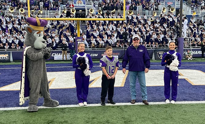 RBI 2025 Football Top Dog Top dog winner and family on JMU's football field next to cheerleaders and the Duke mascot