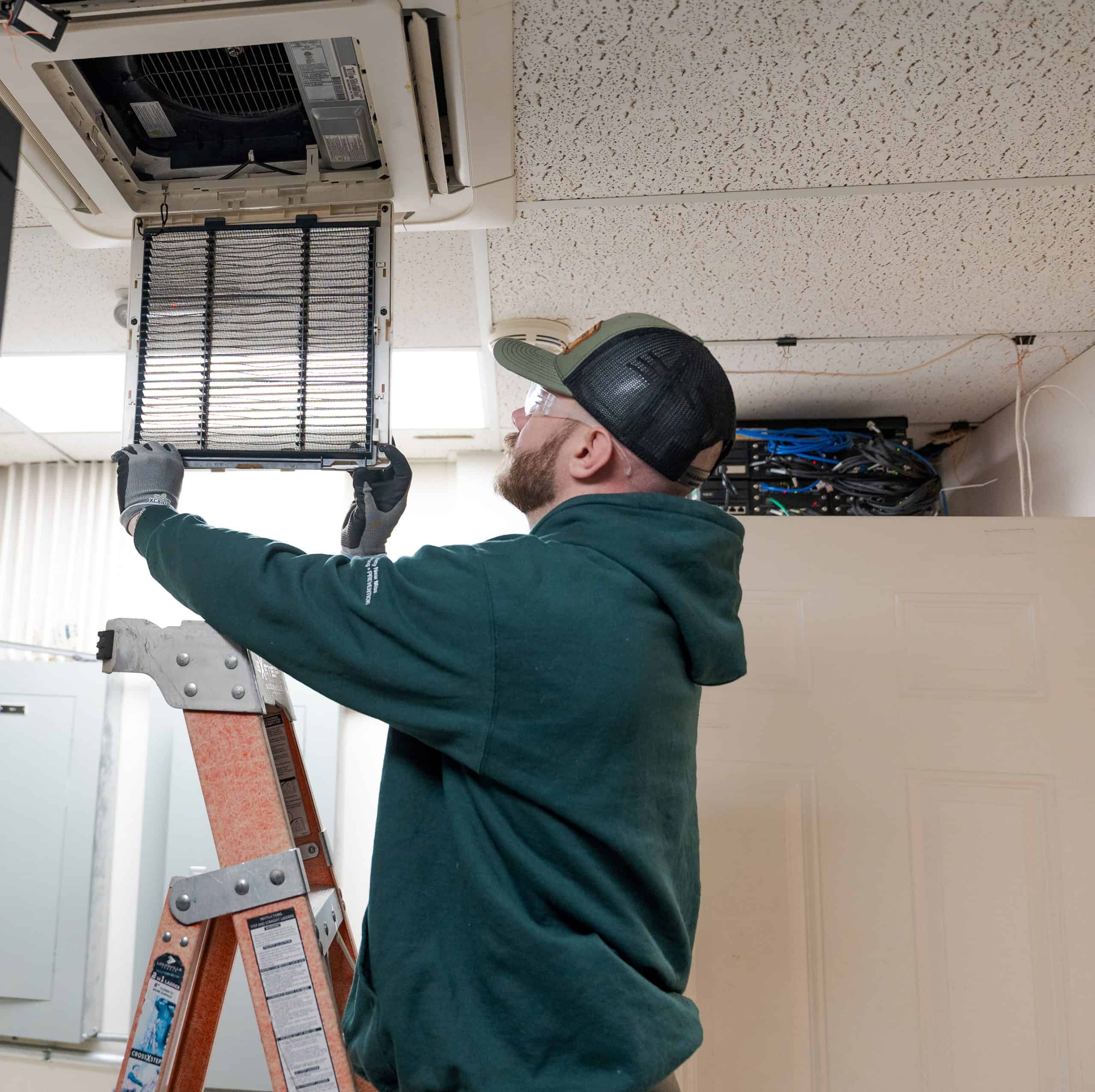 An RBI service technician replacing an HVAC filter in a ceiling vent